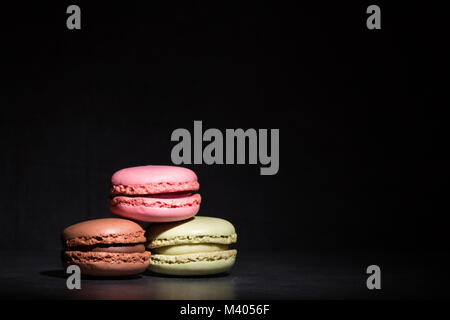 Macarons de bon goût différent dans une tache de lumière sur un fond sombre Banque D'Images