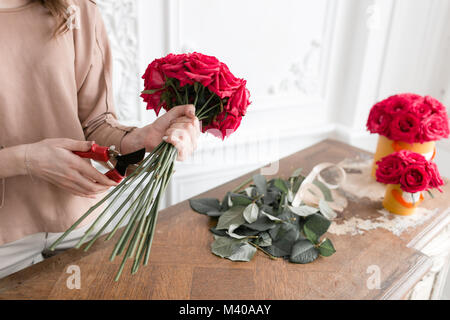 Jeune femme plantes fleuriste organiser dans le magasin de fleurs. Les gens, les entreprises, de la vente et de l'art floral concept. Bouquet de roses rouges Banque D'Images