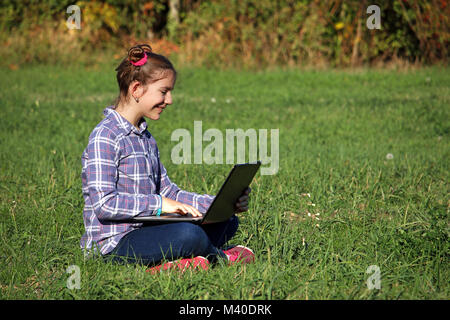 Happy little girl sitting on grass et ordinateur portable de jeu Banque D'Images