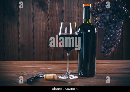 Bouteille et verre de vin rouge, les raisins et le liège sur fond de bois. Banque D'Images