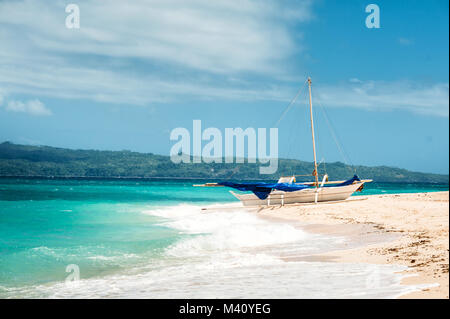 Bateau traditionnel philippin avec voile bleu sur la plage tropicale. Boracay. Lumineux bleu ciel avec les nuages, l'océan avec des vagues, du sable blanc. Banque D'Images