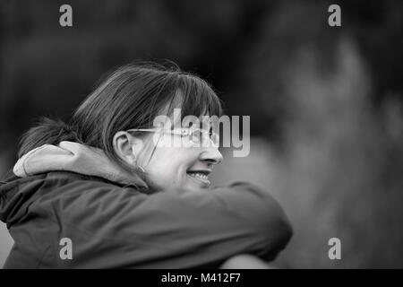 Portrait monolatéral, femme tendance de 50 ans en lunettes, menton posé sur les mains, grand sourire naturel, rêverie. Pleine conscience, temps écoulé, santé mentale. Banque D'Images