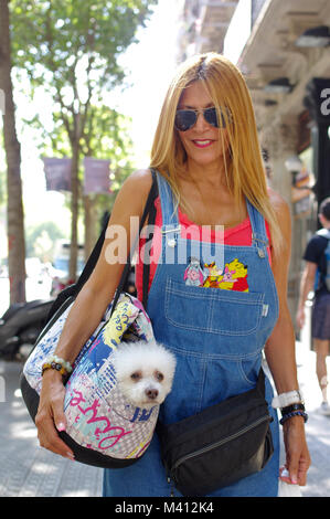 Femme blonde à Barcelone portant un chien maltais dans un sac à bandoulière Banque D'Images