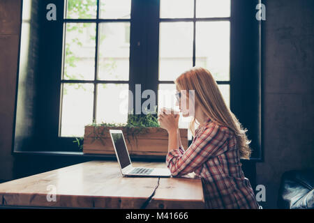 Profil latéral photo de belle blonde wearing concentré chemise décontractée à carreaux ayant un reste de son travail, elle boit du café frais à emporter Banque D'Images