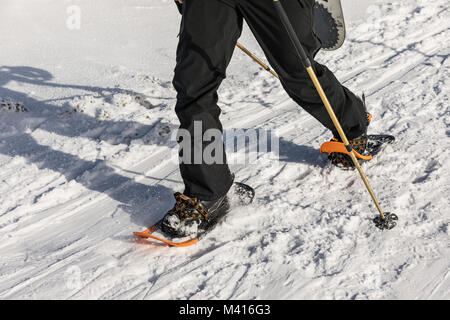 L'homme avec l'orange de la raquette sur le chemin de la neige. L'homme en raquettes avec les bâtons de trekking est la neige dans les montagnes. La raquette est plus souple et le plus haut-p Banque D'Images