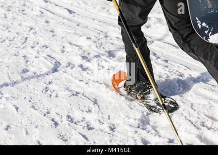 L'homme avec l'orange de la raquette sur le chemin de la neige. L'homme en raquettes avec les bâtons de trekking est la neige dans les montagnes. La raquette est plus souple et le plus haut-p Banque D'Images