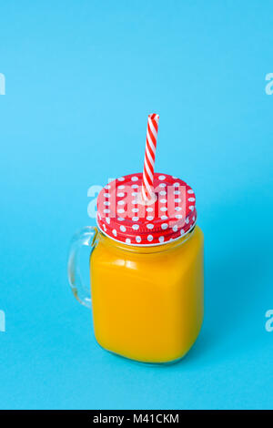 Une orange boissons servis dans un pot Mason de verre avec un couvercle rouge à motifs de points blancs, et une paille dessin rouge et blanc, sur un fond bleu avec Banque D'Images