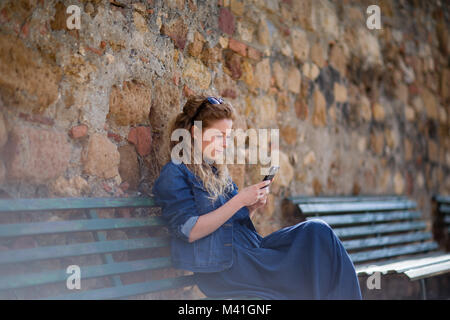 Les jeunes femmes adultes en utilisant smartphone, assis sur un banc Banque D'Images