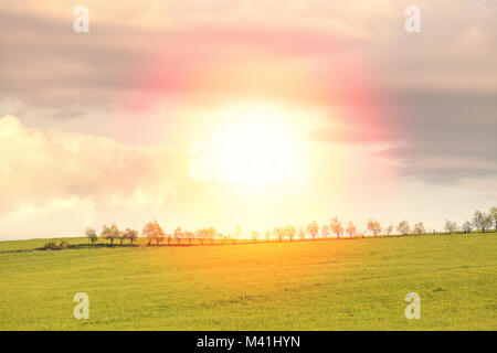 Blue cloudy sky sur green hills et country road with sun shining directement dans camera Banque D'Images
