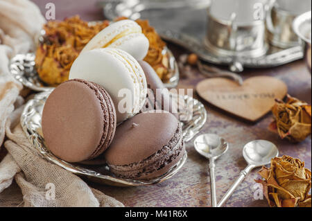 Des petits macarons sur une plaque de métal avec des petites fleurs et un coeur en bois . Focus sélectif. Close up. Banque D'Images