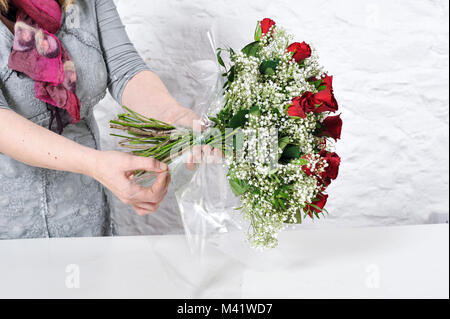 Bois de fleurs d'être organisés pour une occasion spéciale comme la Saint-Valentin. Coupe femme les tiges des fleurs après les arrangeant. Banque D'Images