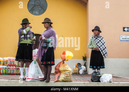 Trois jeunes filles autochtones Comité permanent portant le costume traditionnel avec des sacs de produits à un marché en Equateur Banque D'Images