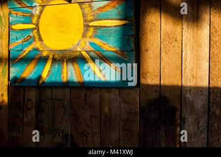 Un simple enfant-comme la peinture d'un soleil jaune sur le côté d'une maison en bois éclairé par la lumière du soleil Banque D'Images