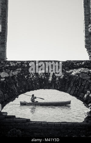 Un pêcheur a vu à travers une fenêtre dans un mur de pierre paddling son bateau en bois Banque D'Images