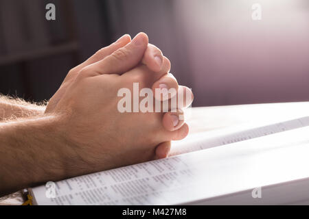 Close-up of Man's priant mains sur la Bible Banque D'Images