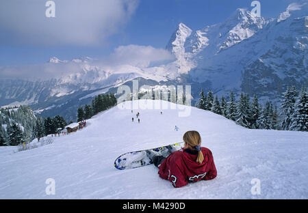 La Suisse. Murren. Saint-divy. Région de la Jungfrau. Snowboard femme assis sur le versant de montagne. Vue du Schilthorn top sur Monch massive. Banque D'Images