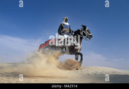 La Tunisie. Oasis de Douz. Désert du Sahara. Man riding horse, dans les dunes de sable fin, nuage, habillé pour festival. Banque D'Images