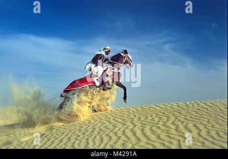 La Tunisie. Oasis de Douz. Désert du Sahara. Man riding horse, dans les dunes de sable fin, nuage, habillé pour festival. Banque D'Images