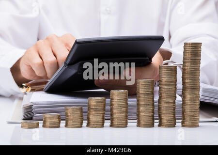 Au milieu du projet de loi d'affaires Le calcul avec la calculatrice et empilés pièces sur Desk In Office Banque D'Images