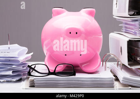 Close-up of Pink Piggy Bank à l'envers sur des documents avec les lunettes sur 24 Banque D'Images