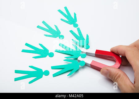 Close-up of a person's Hand Holding Red Horseshoe aimant qui attire des candidats de papier sur fond blanc Banque D'Images