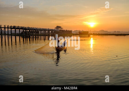 Un pêcheur sur un bateau, c'est le tirant hors de son filet à côté du lac Taungthaman U Bein Bridge au lever du soleil Banque D'Images