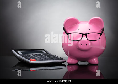 Close-up of Pink Piggy Bank et Calculatrice sur fond gris Banque D'Images