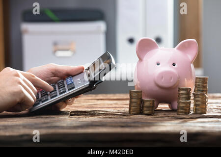 L'homme d'Hand Using Calculator Laughing And Piggy Bank Le bureau en bois Banque D'Images
