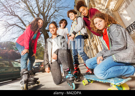 Vue à angle faible de jeunes garçons et filles avec des planches à roulettes ou rollers Standing together at city street Banque D'Images