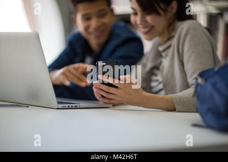 Les étudiants à la recherche en bibliothèque dans smartphone Banque D'Images