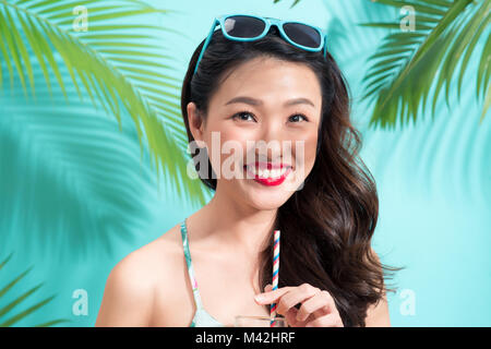 Young Asian woman boissons jus provenant de plus de verre bleu fond coloré Banque D'Images