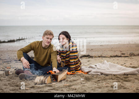 Jeune couple toasting guimauves sur feu de camp Banque D'Images