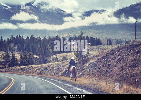 Vintage photo aux couleurs d'un cheval femelle cavalier dans un chapeau de cowboy sur une route, USA. Banque D'Images