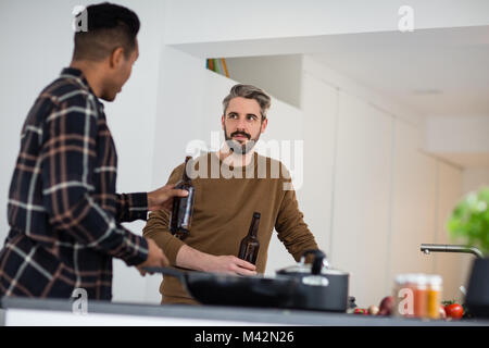 Amis de sexe masculin ayant une bière tout en cuire un repas Banque D'Images