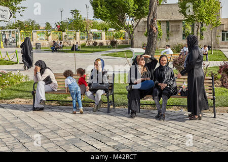 Téhéran, Iran - avril 28, 2017 : in un hijab communiquer par téléphone et les uns avec les autres sur un banc dans un parc public, les enfants jouent à proximité. Banque D'Images