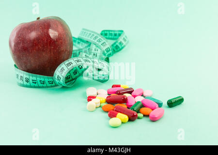 Concept de suivre un régime avec les produits de apple, ruban à mesurer et de pilules ou de comprimés sur fond vert médical Banque D'Images