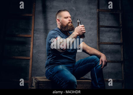 Homme tatoué barbu de boire de la bière à partir d'une bouteille. Banque D'Images