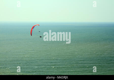 Vol parapente rouge dans le ciel bleu au-dessus de l'océan. Banque D'Images