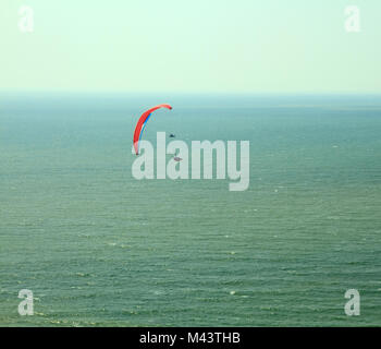 Vol parapente rouge dans le ciel bleu au-dessus de l'océan. Banque D'Images