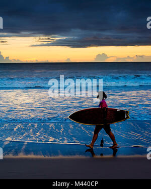 Surfgirl marche sur la plage avec une planche de surf au coucher du soleil. L'île de Bali