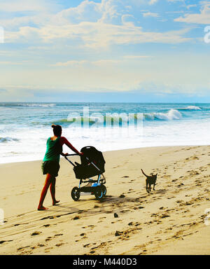 Femme avec une poussette et un chien à pied par la plage. L'île de Bali, Indonésie Banque D'Images