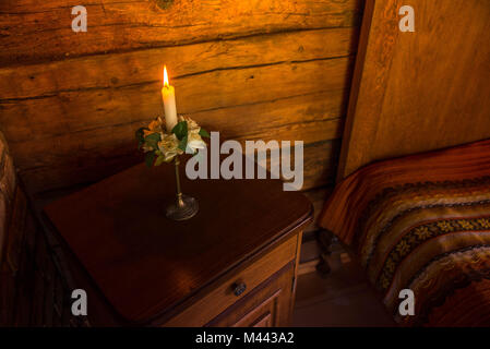 Bougie allumée dans chandelier avec white rose Décorations, fleurs et feuilles vertes debout sur une table de nuit rustique à côté du lit dans la chambre d'antiquités Banque D'Images