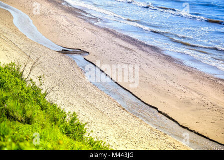 Vue de golden, colorée, abstract sea coucher du soleil au bord de mer. Un ruisseau s'écoule entre l'eau salée de l'océan, des dunes, du sable, des rochers et de la plage. Pont en bois, un s Banque D'Images