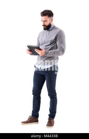 Homme barbu sérieux ou enseignant la lecture des feuilles de carnet. La pleine longueur du corps portrait isolé sur fond blanc studio. Banque D'Images