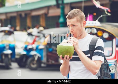 Jeune homme de boire un verre de coco contre tuk tuk taxi. Dans la rue touristique de Bangkok, Thaïlande. Banque D'Images