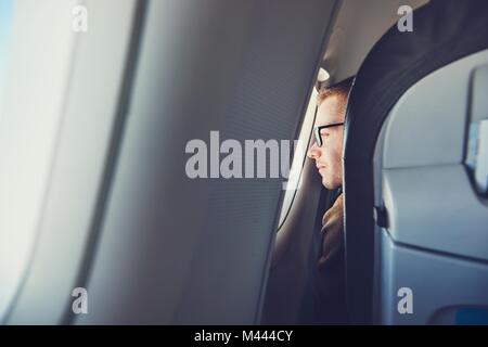 Voyages en avion confortable. Jeune homme (meilleur) avec des lunettes à la recherche d'une fenêtre pendant le vol. Banque D'Images