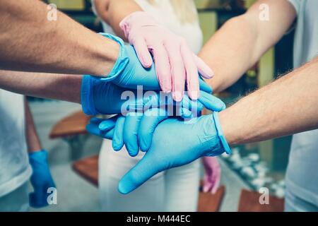 Le travail d'équipe des médecins à l'hôpital. Les mains de quatre hommes en bleu gants de protection et d'une femme en rose gants. Thèmes de santé, la coopération, la confiance et la réussite Banque D'Images