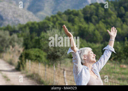 Senior woman, à l'extérieur, bras levés, expression sans souci Banque D'Images