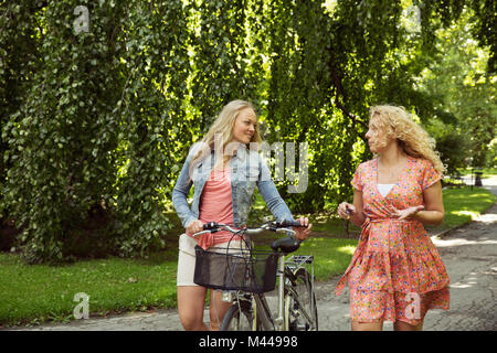 Amis marchant avec des bicyclettes chatting Banque D'Images