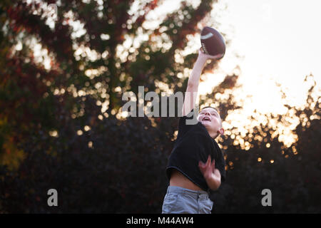 Boy practicing football américain dans jardin atteindre pour attraper ball Banque D'Images